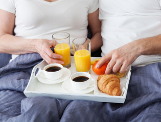 Obraz na płótnie Canvas Portrait of happy playful couple relaxing in comfortable cozy bed looking at each other, cheerful man and woman having fun posing. Drink orange juice while covering their shoulders with blanket.