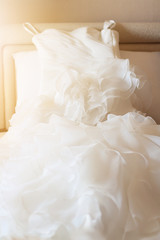 Wedding dress lying on the white bed with beautiful sun light in hotel room. Valentines day and love for celebration concept.