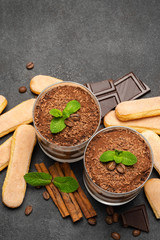Classic tiramisu dessert in a glass and savoiardi cookies on dark concrete background