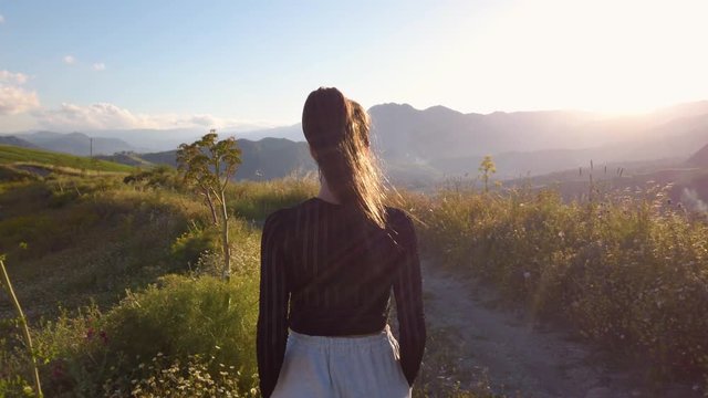Ragazza con tuta grigia e maglia nera balla a ritmo di musica in mezzo a una strada in campagna tra la natura. Tramonto del sole sullo sfondo.