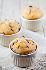 Homemade fresh muffins on ceramic white bowls on linen napkin on rustic wooden table.