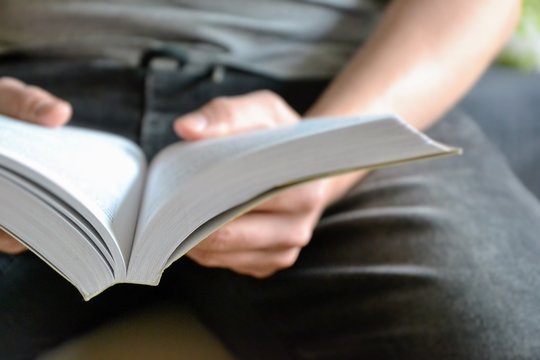 Man is reading a book, close up, vintage style. Book opened for reading. Young man is reading a book.Close-up picture of hand holding a book. Out of focus, intentionally blurred