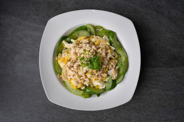 Fried cucumber with chicken egg in white dish on concrete table.