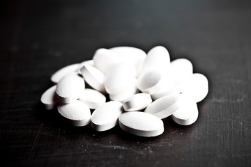 Pile of white drug pills laying on black board background.