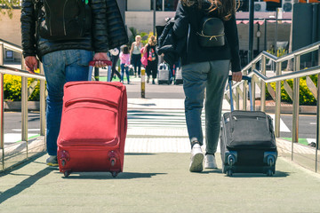 Family taking a plane. Friends returning from vacation walk at airport departures. Adult and teen leaves happy for carefree days of break. Back view of two people traveling with holidays luggages