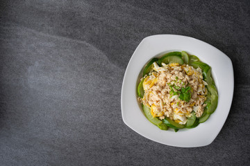 Fried cucumber with chicken egg in white dish on concrete table.