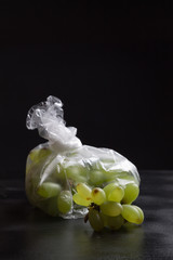 Grapes in a plastic bag on a dark background. The image shows the harmful effects of plastic bags...