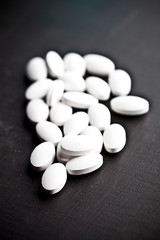 Pile of white drug pills laying on black board background.