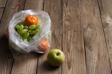 Fruits(tangerines,apples,grapes) in a plastic bag on a natural wooden background. The image shows the harmful effects of plastic bags on food.