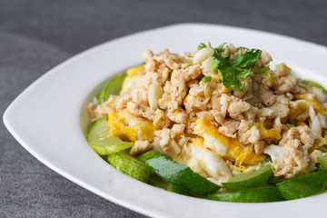 Fried cucumber with chicken egg in white dish on concrete table.