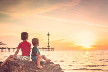 Two boys sitting on the rock at the beach at sunset