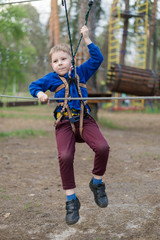 A little boy is training in a rope park. The child climbs the obstacle course. Active recreation in the park in the fresh air.