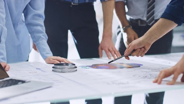 Industrial Engineering Facility: Close-up on Hands of Group of Engineers, Technicians and Specialists on a Meeting, Tracing Lines and Analysing Engine Design Technical Drafts Laying on the Table