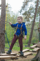 A little boy is training in a rope park. The child climbs the obstacle course. Active recreation in the park in the fresh air.