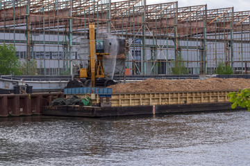 Ein Bagger entlädt Holzspäne von einem Schubleichter