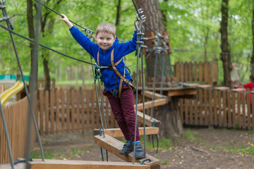 A little boy is training in a rope park. The child climbs the obstacle course. Active recreation in the park in the fresh air.