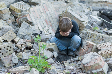 Little boy near the destroyed house. Child trouble, loneliness concept.