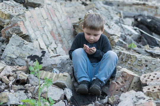 Little boy near the destroyed house. Child trouble, loneliness concept.