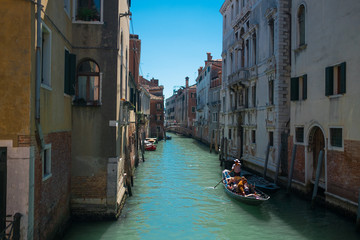Fototapeta na wymiar view of traditional venetian gondola boat in water canal with couple of lovers taking a romantic and relaxing ride during a sunny summer day