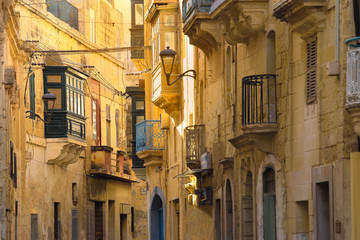 Selective focus on green balcony, traditional houses building facade with sandstones and covered balconies in Malta, Valletta,
