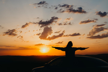 Silhouette of a girl at sunset in the summer, the girl riding in the car with his hands apart