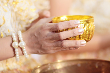Woman hand hoding Gold cup for Pour water in conch shell on glod tray in tradition Thai wedding ceremony
