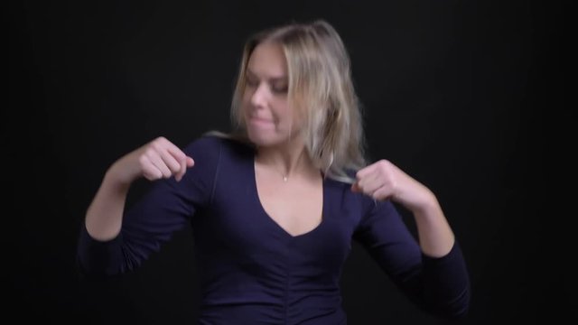 Happy middle-aged blonde businesswoman in blue blouse dancing actively and emotionally on black background.