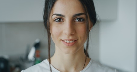 Portrait of an young woman is looking and smiling in the camera in the kitchen.