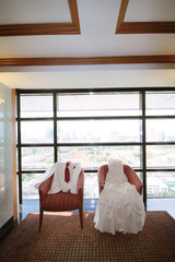 Wedding Dress and suit lying on armchair in wedding ceremony. Groom and Bride clothes concept.