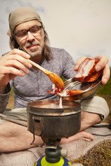 Mature man on trip in summer wilderness preparing food
