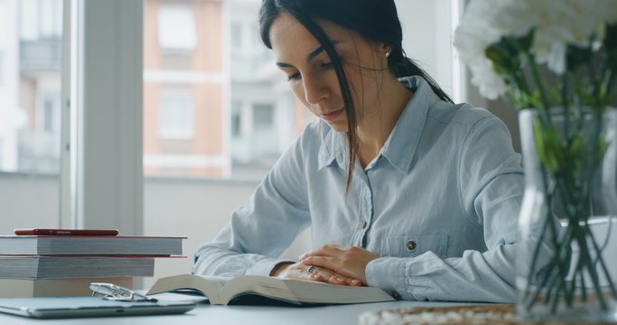 Portrait of a young woman is reading a book for exam preparation at home.