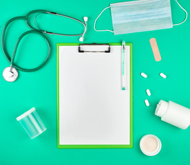 Fototapeta na wymiar paper holder with empty white sheets, medical stethoscope, pills on a green background