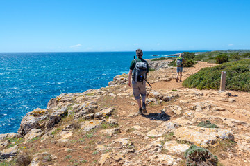 Hikers on a coastal path by the sea in Menorca, Balearic islands, Spain