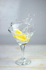 Martini glass with lemon slice splash on light background