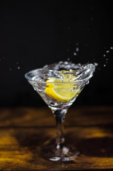 Martini glass with lemon slice splash on dark background