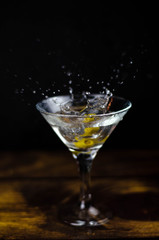 Martini glass with olive splash on dark background