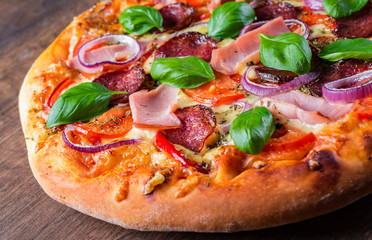 Pizza with Mozzarella cheese, ham, tomato sauce, salami, onion, pepper, Spices and Fresh basil. Italian pizza on wooden table background