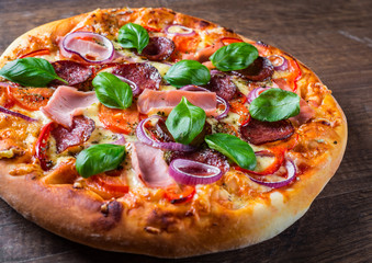 Pizza with Mozzarella cheese, ham, tomato sauce, salami, onion, pepper, Spices and Fresh basil. Italian pizza on wooden table background