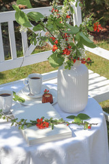 Enjoying coffee time in the garden. White table with coffee, caneles and flowers served in the garden
