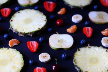 Various fruits and fruit slices on dark background: pineapple,apple, strawberry, banana, blueberry, cherry and tangerine. Selective focus.