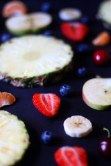 Various fruits and fruit slices on dark background: pineapple,apple, strawberry, banana, blueberry, cherry and tangerine. Selective focus.