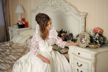 beautiful girl in a long white dress sitting on the bed