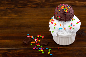 plate of vanilla and and chocolate ice cream scoop swith sprinkles and waffle cones on wooden...