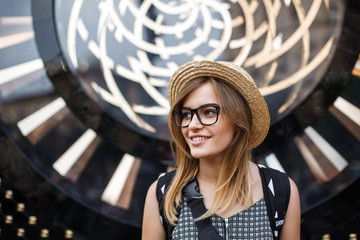 Happy traveling fashion girl in sunny downtown. Straw hat and backpack.