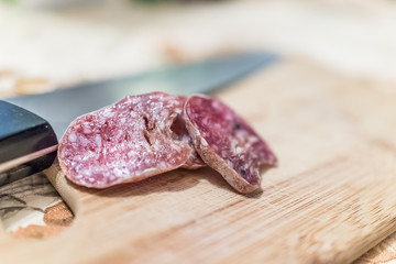 Hard salamai slices on cutting board by blurred background of knife by meat