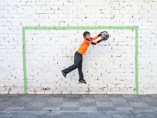goalkeeper catches the ball in front of a goal painted on the wall