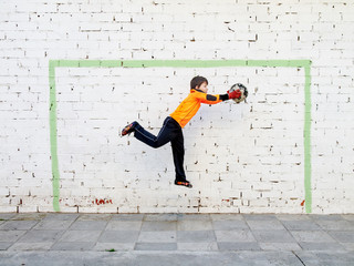 goalkeeper catches the ball in front of a goal painted on the wall