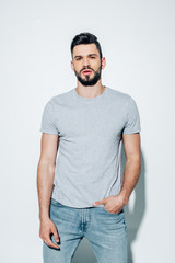 handsome bearded man looking at camera and standing with hand in pocket on white