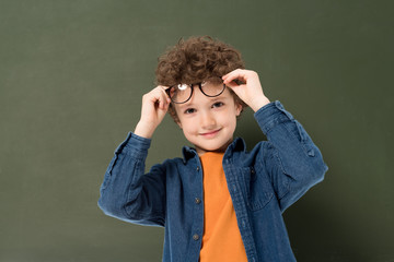 smiling curly kid with glasses looking at camera isolated on green