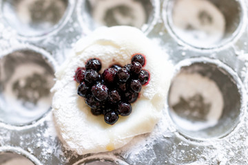 Piece of mochi sticky glutinous rice cake dusted with starch flour to make dessert in muffin pan tin, with heart shape blue blueberry fruit filling